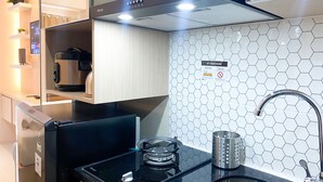 A modern kitchen with a black induction cooktop, a stainless steel range hood, and a sink with a hexagonal tile backsplash. - Modern Look And Homey Studio Apartment At Transpark Juanda Bekasi Timur (Bekasi)