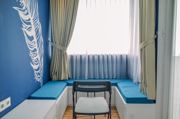 Una habitación con una pared azul, una ventana con cortinas azules, una silla blanca y un banco con cojines azules.