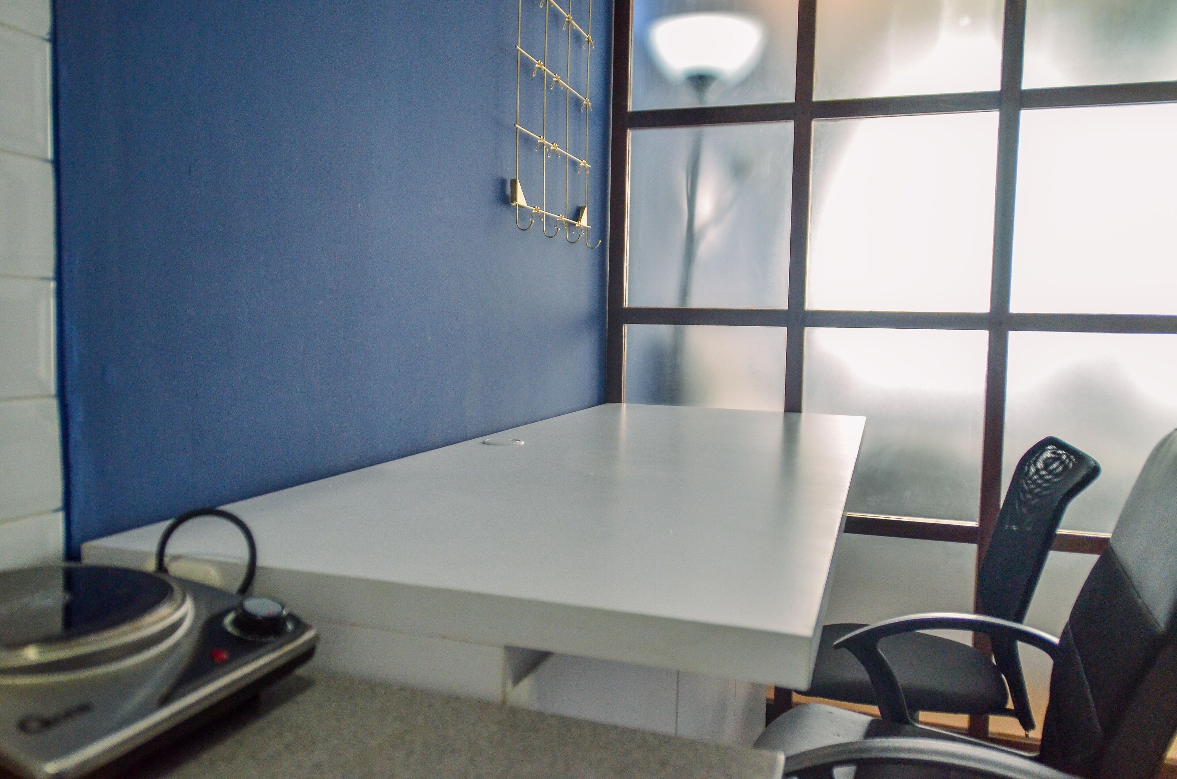 A room with a white table, a black chair, a blue wall, and a window with a grid pattern.