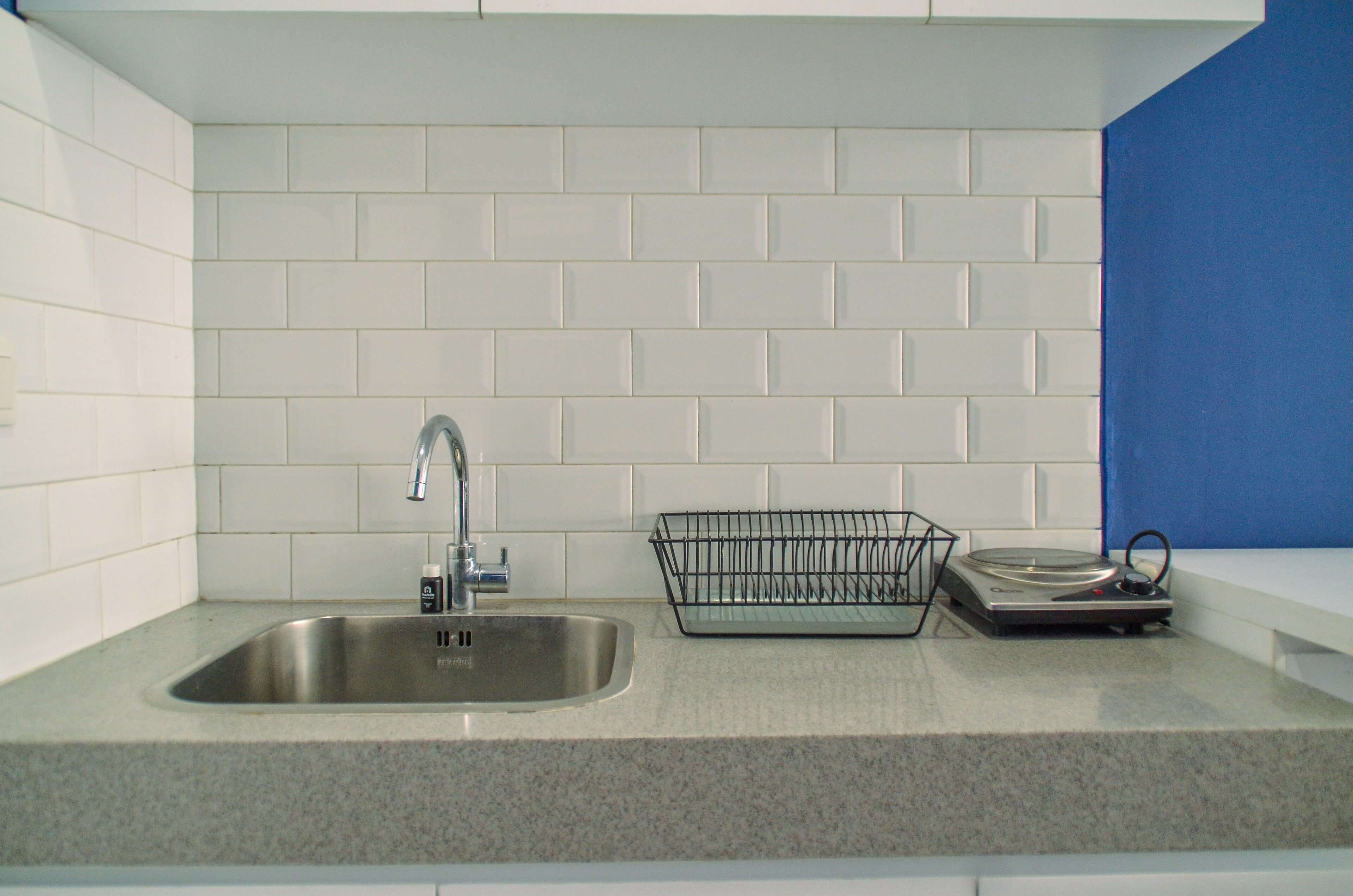 A kitchen with a stainless steel sink, a dish rack, and white subway tiles on the wall.