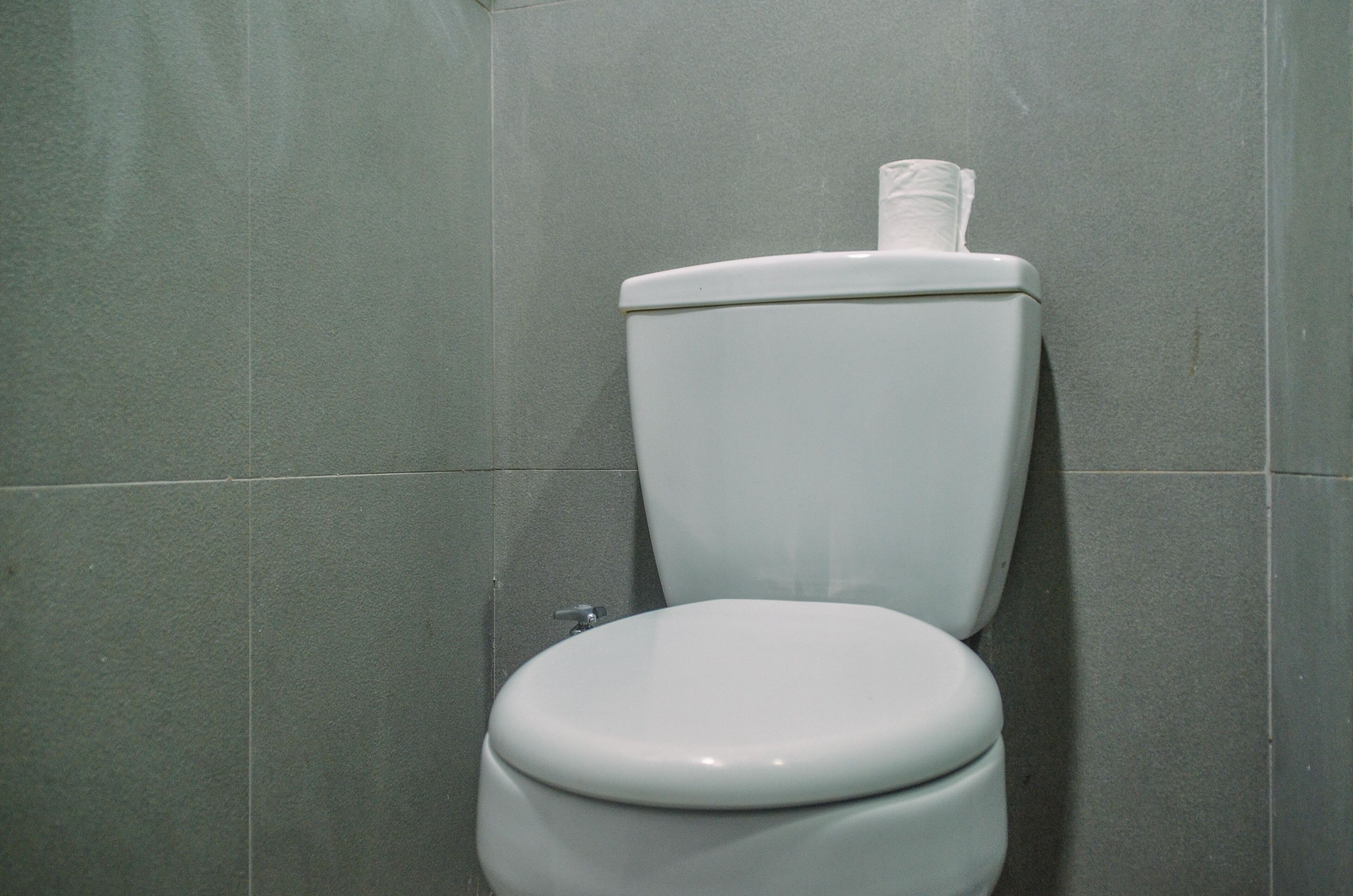 A standard white toilet in a bathroom with grey tiles on the walls.