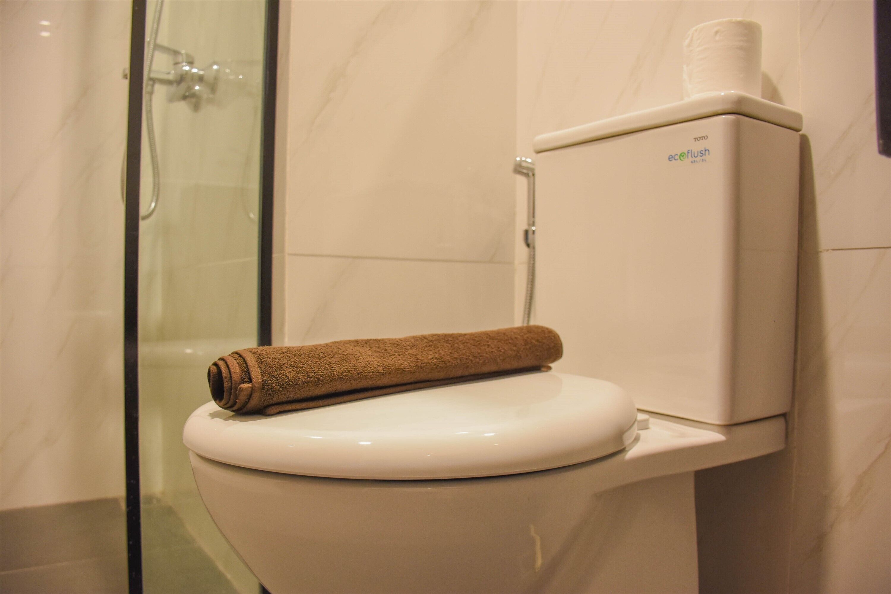 A toilet with a towel on the lid and a toilet paper holder on the wall.