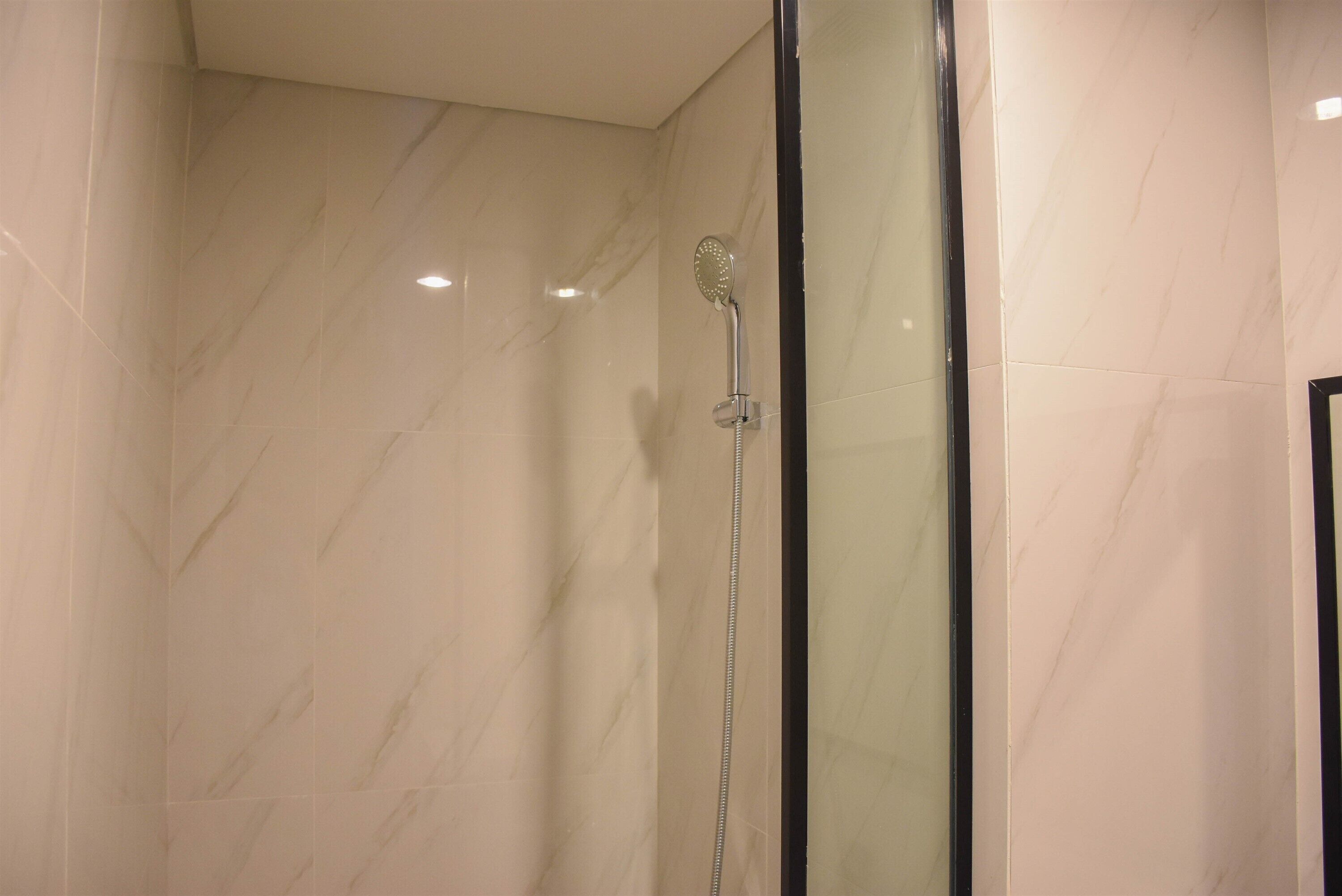A modern bathroom with a glass shower enclosure and marble walls.