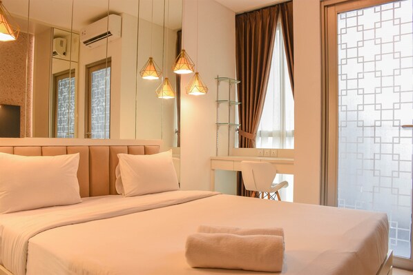 Relax in a spacious room with a large bed, desk, and mirror, offering a comfortable workspace and a view of the outside.