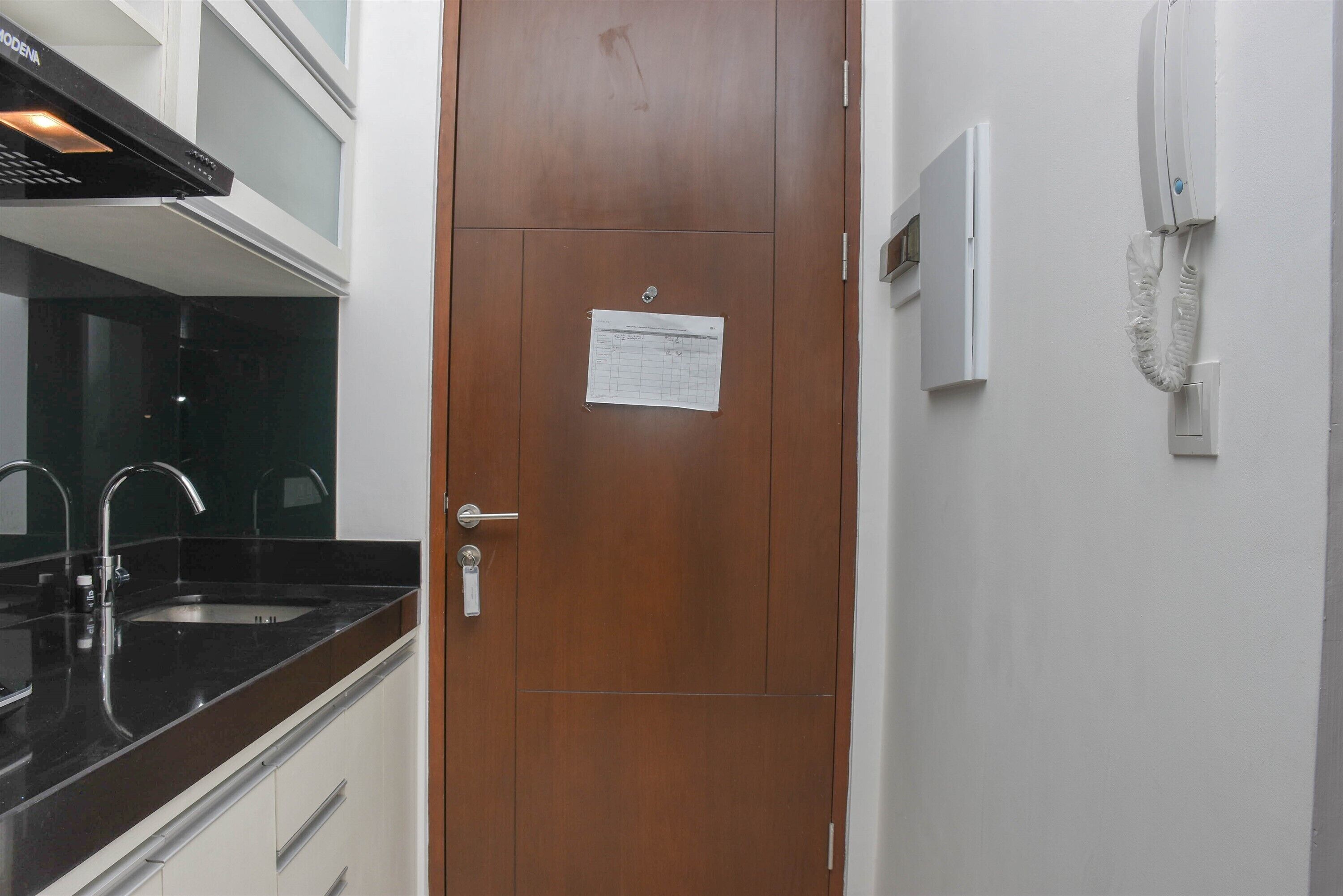 A kitchen with a wooden door, a sink, and a paper note attached to the door.