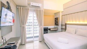 A hotel room with a bed, TV, air conditioning unit, and a window with curtains. - Modern Look Studio Lrt City Sentul - Royal Sentul Park Apartment (Bogor)