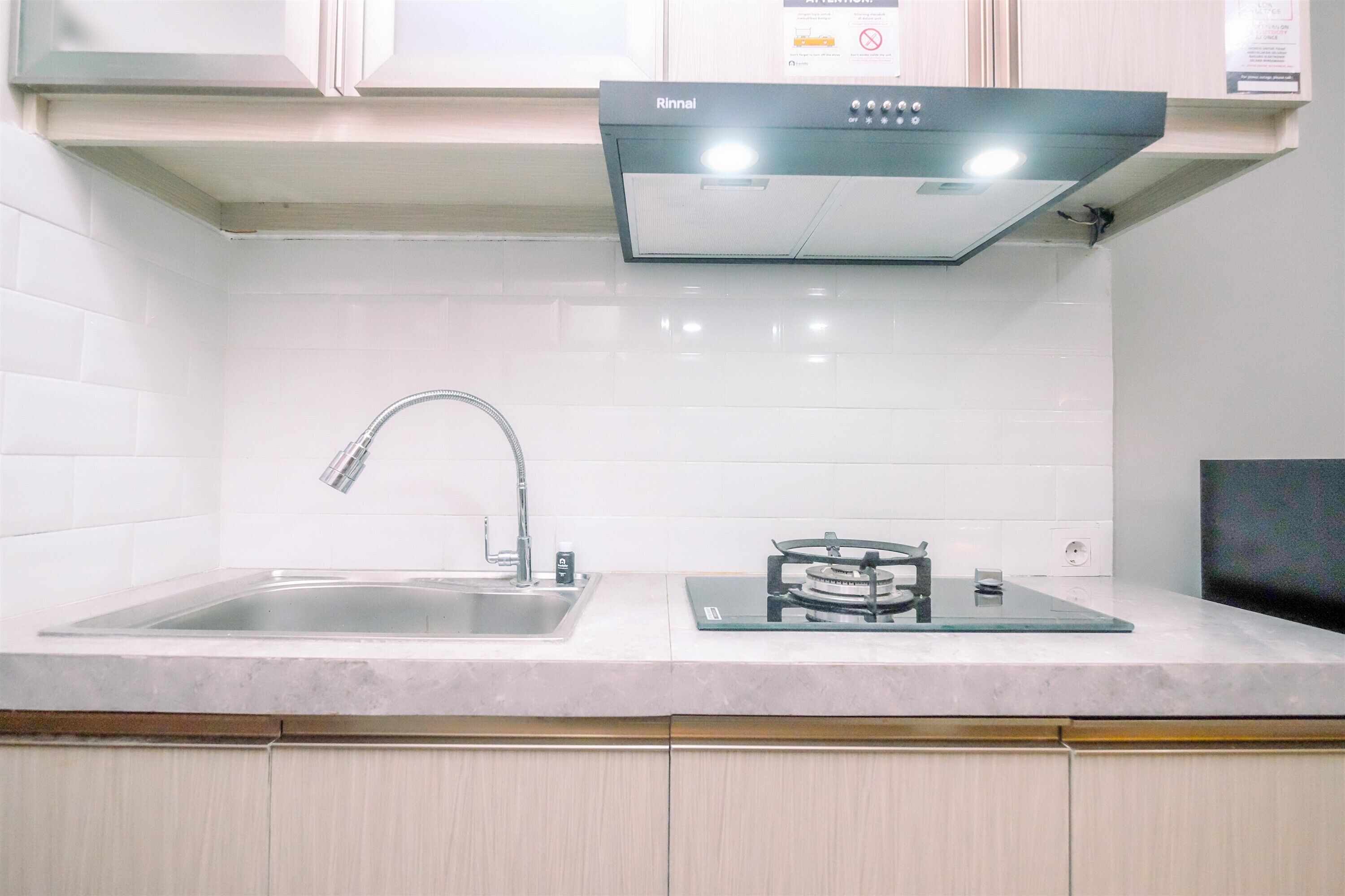 A kitchen with a stainless steel sink, a Rinnai range hood, and white tiled walls.