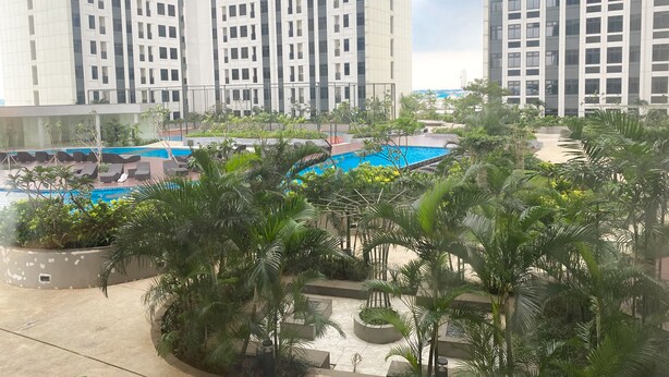 Un hotel moderno con piscina sul tetto, circondato da vegetazione lussureggiante e alti edifici sullo sfondo.