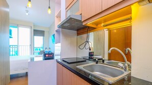 A modern kitchen with a black countertop, stainless steel sink, and wooden cabinets. There are overhead lights and a window in the background. - Minimalist Studio With Great City View At Tifolia Apartment (Jakarta)
