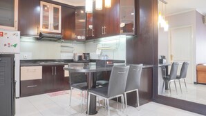 A modern kitchen with dark wooden cabinets, a black countertop, and a dining area with four chairs. - Cozy And Simply Look 2Br At 12Nd Floor Puri Garden Apartment (Jakarta)