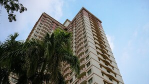 A tall residential building with multiple balconies and a palm tree in the foreground. - Cozy And Simply Look 2Br At 12Nd Floor Puri Garden Apartment (Jakarta)