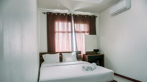 A neatly made bed with white linens, a wooden headboard, and a pair of rolled towels on the footboard.