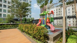 A playground with slides and climbing structures, surrounded by greenery and residential buildings.
