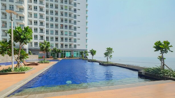 A swimming pool with clear blue water, surrounded by a tiled deck and small trees.