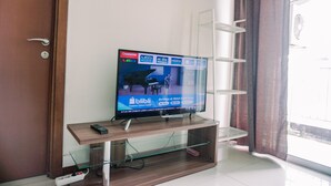 A television on a wooden stand with a remote control, a glass shelf below, and a white door with a silver handle.