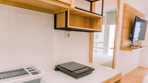 A modern hotel room with a wooden bed, a TV mounted on the wall, and a small table with a portable heater. - Comfy Studio At 30Th Floor Tokyo Riverside Pik 2 Apartment (Teluknaga)