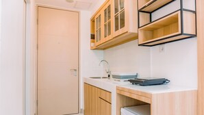 A compact kitchen with wooden cabinets, a built-in sink, and a compact refrigerator. - Comfy Studio At 30Th Floor Tokyo Riverside Pik 2 Apartment (Teluknaga)