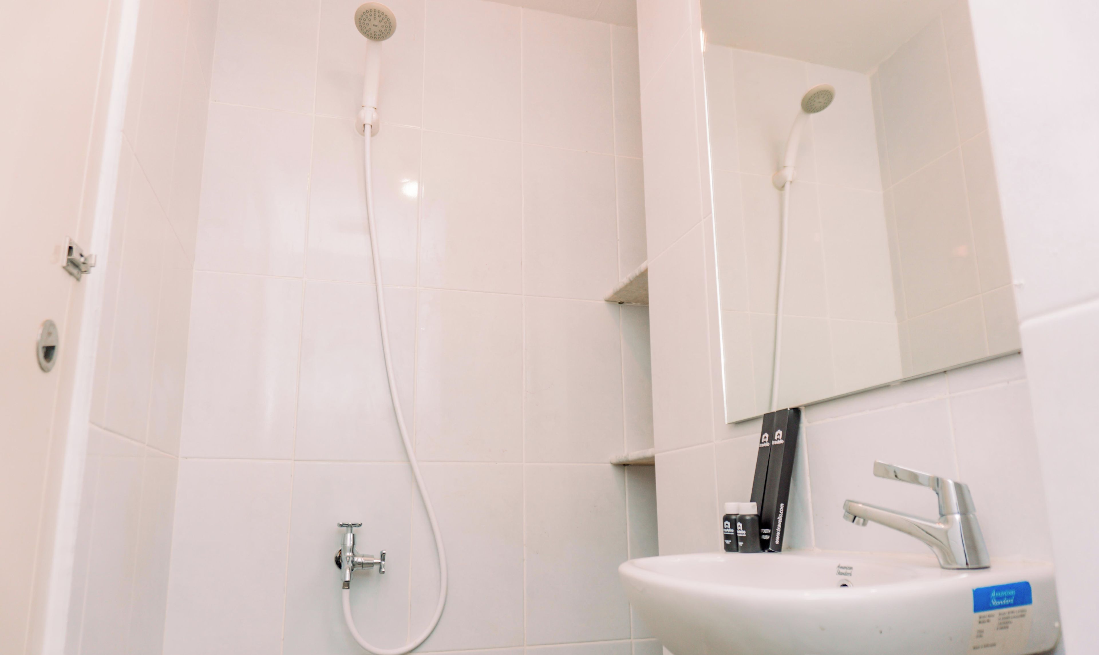 A bathroom with white tiles, a sink, a mirror, and a shower.