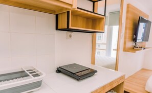Quarto de hotel moderno com cama de madeira, TV fixada na parede e uma pequena mesa com aquecedor portátil.