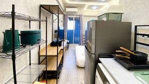 A narrow hallway with kitchen appliances, including a refrigerator, a stove, and shelves with pots and pans. - Fully Furnished And Homey Studio Grand Kamala Lagoon Apartment (Bekasi)