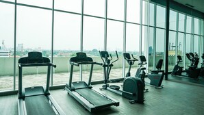 Une salle de sport équipée de tapis de course, de vélos elliptiques et de vélos d’appartement, avec de grandes fenêtres offrant une vue sur la ville.