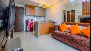 A modern living room with a red sofa, a TV, and a kitchen area with wooden cabinets and a marble countertop. - Nice And Comfort 2Br Apartment At Transpark Cibubur (Depok)