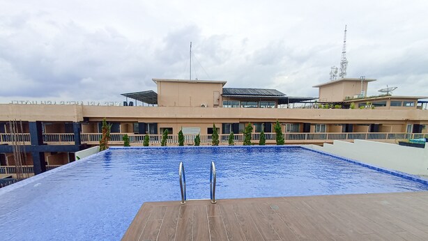 A swimming pool with wooden deck, surrounded by buildings with balconies and satellite dishes.