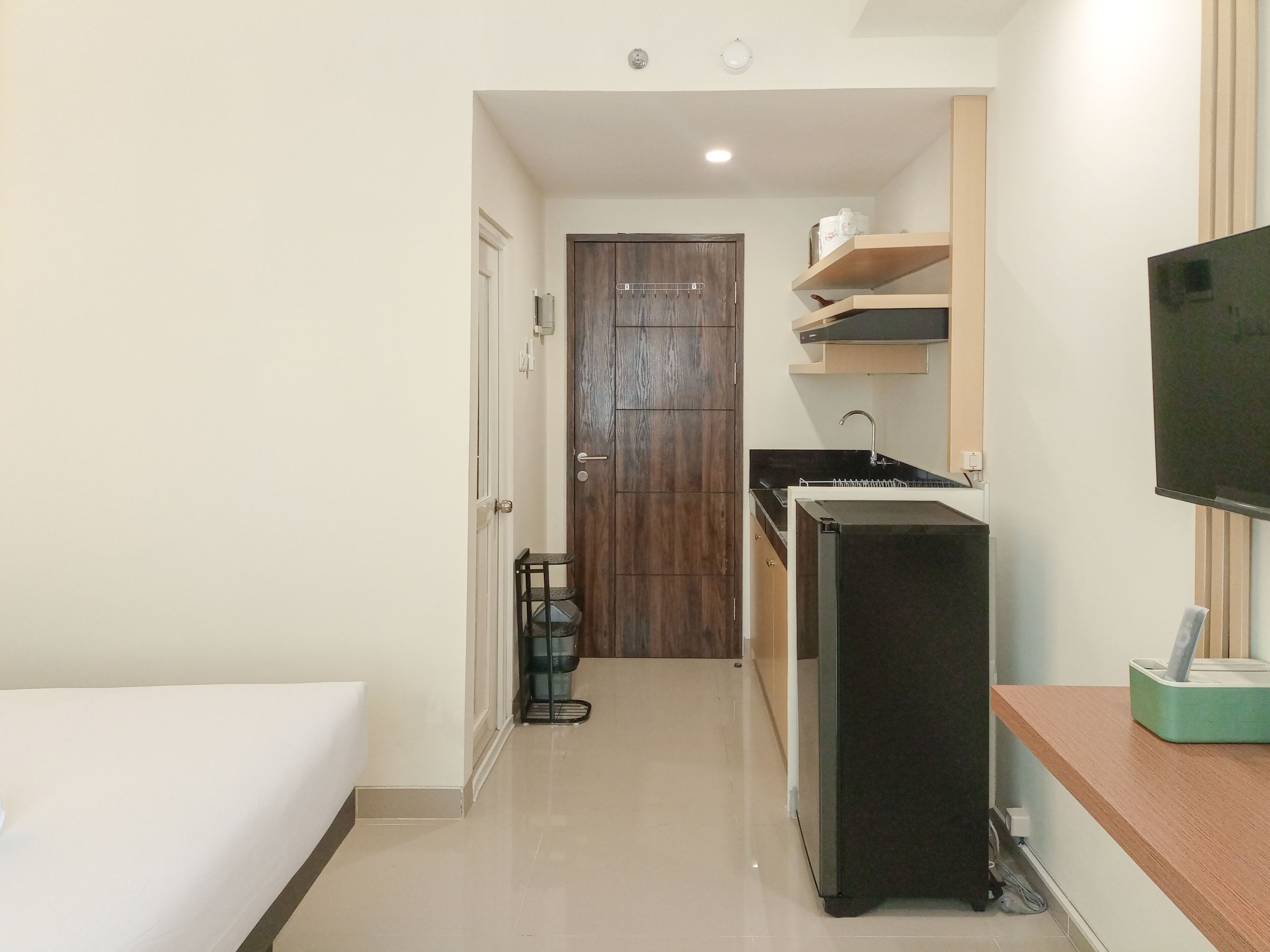 A hotel room with a bed, a small kitchenette, a TV, and a door leading to the hallway.