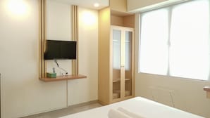 A hotel room with a bed, a TV mounted on the wall, a wardrobe, and a window.