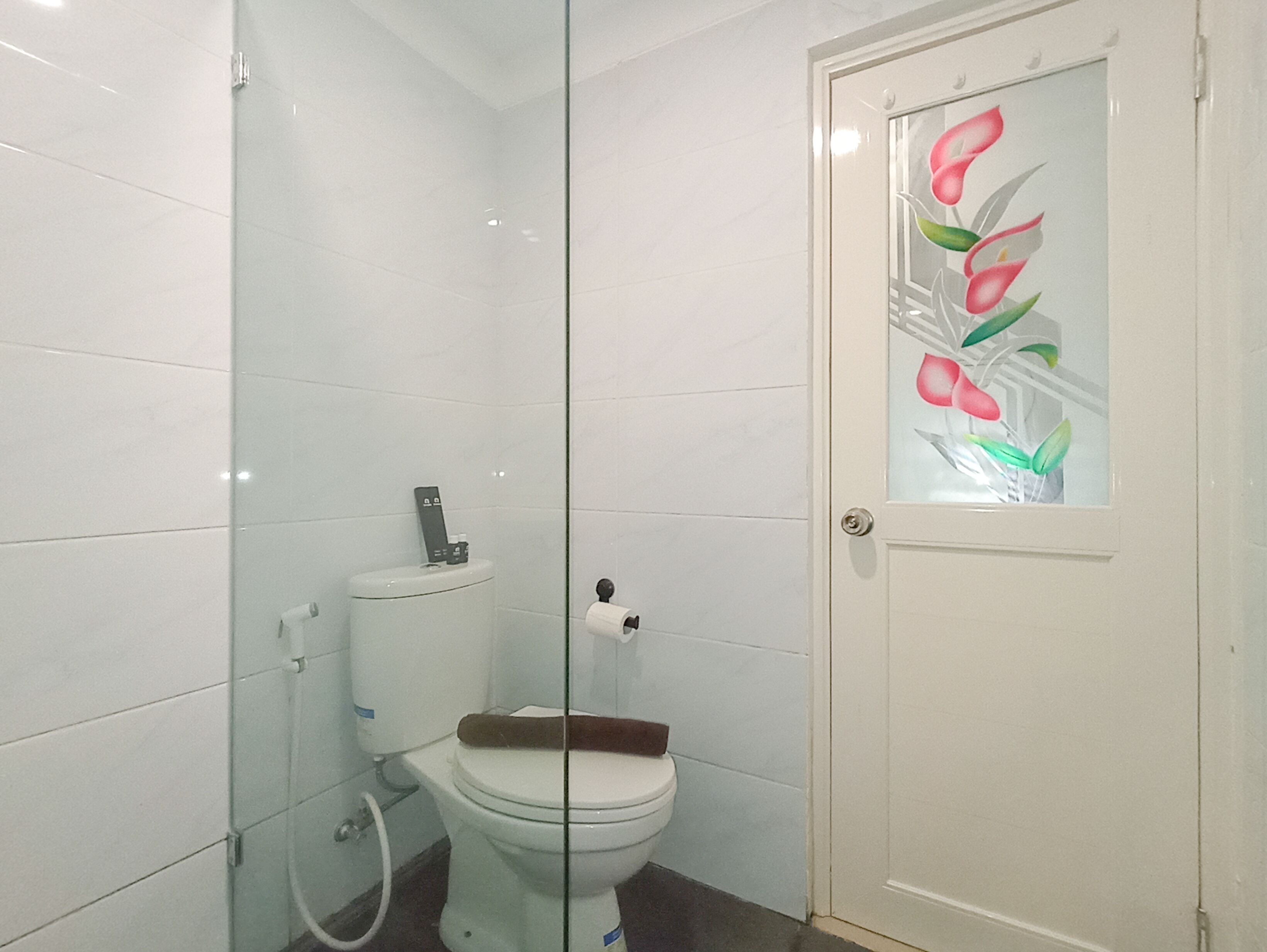 A bathroom with a toilet, a glass shower enclosure, and a door with a floral design.