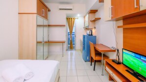 Quarto de hotel com cama, escrivaninha, televisão e armário.