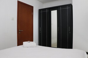Une chambre avec une porte en bois, une armoire noire avec des miroirs et un lit blanc.