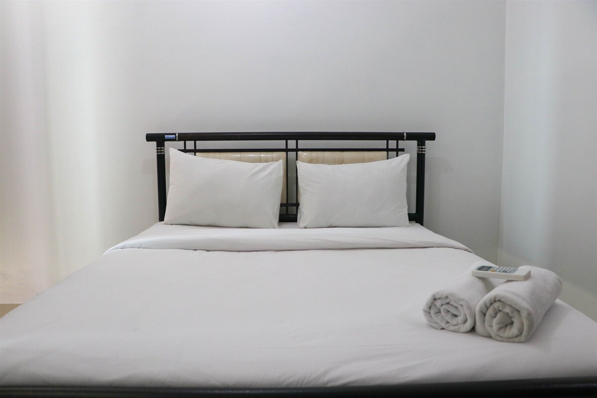 Una cama bien tendida con sábanas blancas, cabecero de metal negro y dos toallas enrolladas a un lado.
