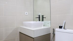A modern bathroom with a white sink, a glass shower enclosure, and a toilet with toiletries on top.