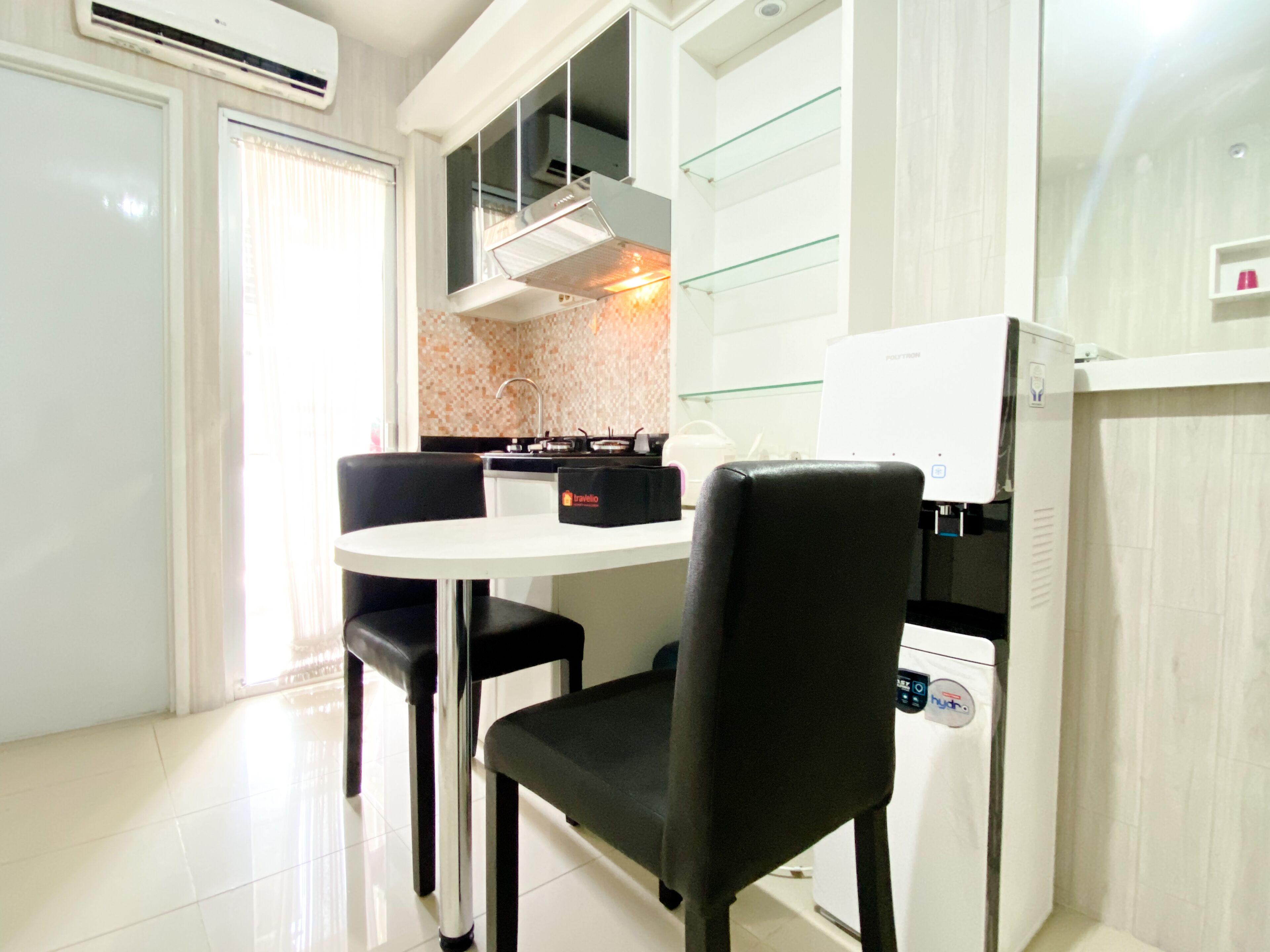 Cocina compacta con encimera blanca, sillas negras, estufa integrada y refrigerador.