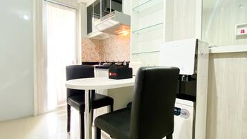 Cocina compacta con encimera blanca, sillas negras, estufa integrada y refrigerador.