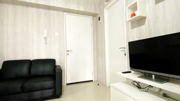 Uma sala de estar com um sofá preto, um móvel branco para entretenimento com uma TV de tela plana e uma porta branca.