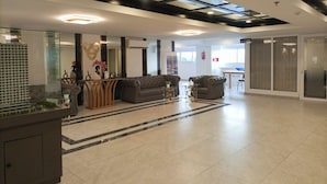 Eine großzügige Lobby mit modernem Design, ausgestattet mit einer großen Couch, einem Empfangstresen und einer Glastrennwand.