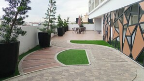 Eine Dachterrasse mit gewundener Wege, Blumentöpfen, einem Tisch mit Stühlen und Blick auf die Skyline.