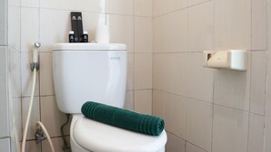 Des toilettes blanches avec une serviette verte posée dessus, un bidet et un sèche-mains fixé au mur.