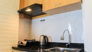A compact kitchen with a black countertop, stainless steel sink, and a kettle.