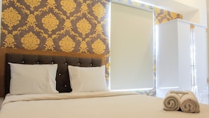 A neatly made bed with a headboard, a window with blinds, and a rolled towel on the bed.