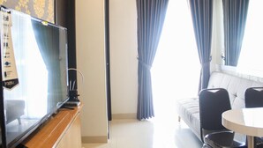 A room with a television on a wooden stand, a sofa, two chairs, and a window with curtains.