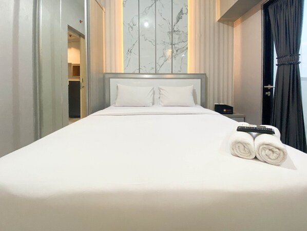 A hotel room with a large bed, white linens, a marble wall, and a remote control on the bed. - Cozy Stay And Tidy 1Br The Alton Apartment (Semarang)
