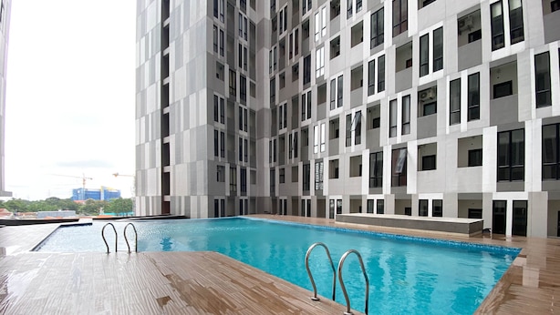 A modern building with a swimming pool, multiple balconies, and a view of construction cranes in the background. - Cozy Stay And Tidy 1Br The Alton Apartment (Semarang)