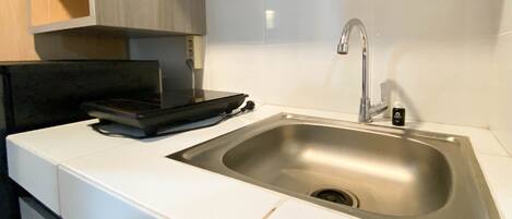 A kitchen with a stainless steel sink, white countertops, and wooden cabinets.