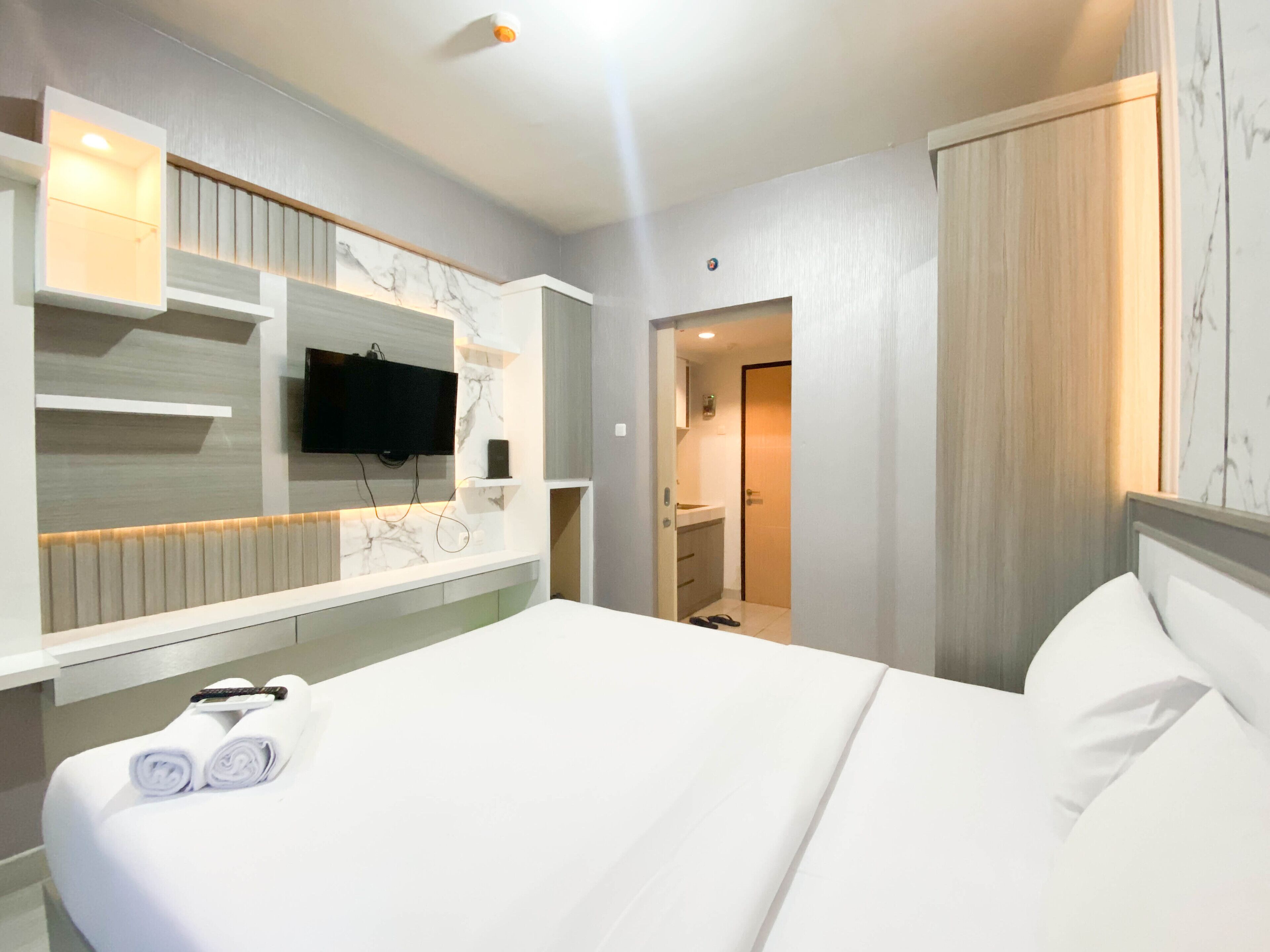 Una habitación de hotel con una cama grande, un televisor de pantalla plana montado en una pared de mármol, un tocador integrado y un vestidor.
