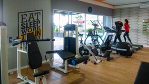 Un gimnasio con diversos equipos de ejercicio, un cartel motivacional y un reloj en la pared.