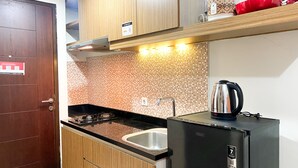 Una cocina compacta con armarios de madera, un refrigerador negro, un hervidor de acero inoxidable y un salpicadero de azulejos.