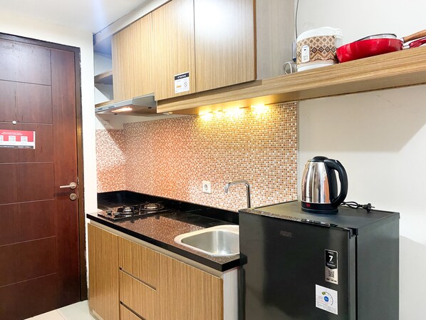 Una cocina compacta con armarios de madera, un refrigerador negro, un hervidor de acero inoxidable y un salpicadero de azulejos.